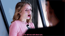 a woman in a pink sweater is talking to another woman in a mirror .