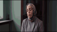 a woman wearing a hijab and a grey coat looks down with her eyes closed