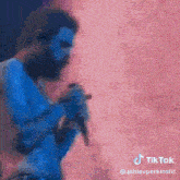 a man with blue paint on his face is singing into a microphone on stage .