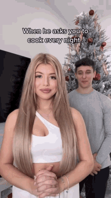 a man and a woman are standing in front of a christmas tree