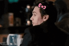 a man with a pink hello kitty bow on his head is sitting at a table .