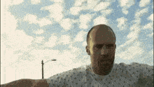 a bald man in a hospital gown is standing in front of a blue sky with clouds .