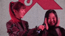 two women are standing next to each other on a stage and one of them is holding the other 's hair .