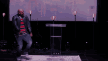 a man in a striped shirt is dancing in front of a large screen