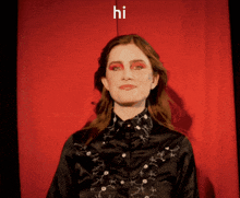 a woman in a black shirt stands in front of a red curtain with the word hi on it