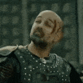 a bald man with a beard and a tattoo on his head is wearing armor .