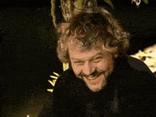 a man with curly hair and a beard is smiling and waving