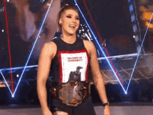 a woman is standing on a stage wearing a wrestling belt and a tank top .