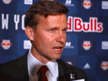 a man in a suit and tie is talking into a microphone in front of a red bulls banner
