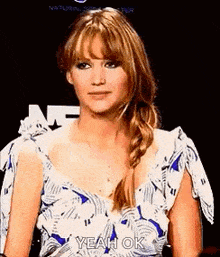 a woman in a blue and white dress is standing in front of a sign that says `` yeah ok '' .