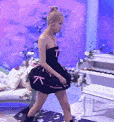 a woman in a black dress with the letter t on it is walking in front of a piano