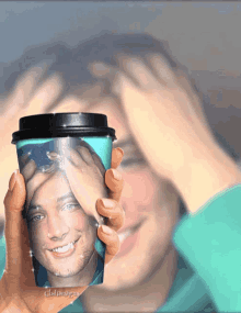 a person holding up a cup with a picture of a man on it