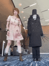 a woman in a pink dress stands next to a man in a black coat