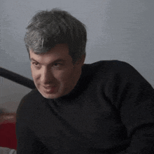 a man wearing a black sweater looks at the camera