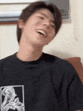 a young man wearing a black t-shirt is laughing with his mouth open