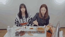 two girls sit at a table with a twice logo on the bottom
