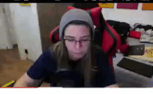 a woman wearing a beanie and glasses is sitting in a red chair .