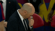 a bald man in a suit and tie is holding a pen to his nose