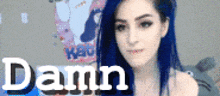 a woman with blue hair is standing in front of a wall that says damn