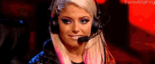 a woman wearing headphones and a microphone is smiling and looking at the camera .
