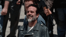 a man with a beard wearing a leather jacket is smiling in a crowd .