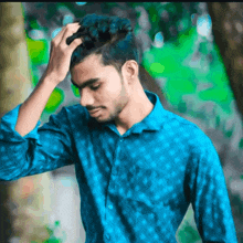 a young man in a blue shirt holds his hand to his forehead