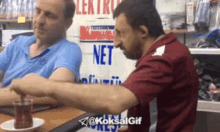 two men are sitting at a table with a sign that says net