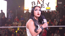 a woman in a wrestling ring holds a microphone in front of a large screen that says bayley