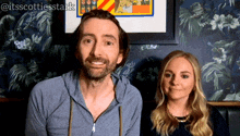 a man and a woman are smiling in front of a floral wall with the hashtag itsscottiesstark