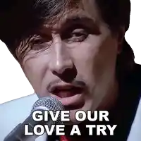 a man singing into a microphone with the words give our love a try written below him