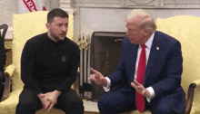 a man in a suit and tie sits next to a man in a black shirt that says rm on it