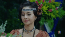 a woman wearing a headband and a necklace is standing in front of a flower arrangement .