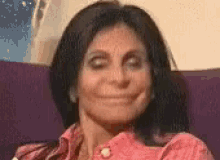 a woman is smiling while sitting in a chair and wearing a pink shirt .