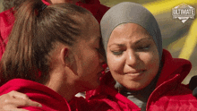 a woman in a hijab is hugging another woman in a red jacket that says ultimate challenge