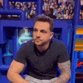 a man in a black shirt with a tattoo on his arm is sitting in front of a crowd that is watching a show