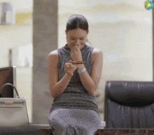 a woman in a gray dress is sitting on a marble counter looking at her phone