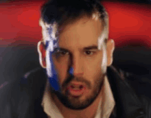 a man with a beard is wearing a leather jacket and a white shirt and is looking at the camera .