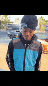 a man wearing a blue jacket and a black beanie is standing in front of cars .