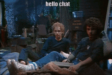 a man in a suit is standing next to another man who is sitting at a desk and the words hello chat are on the screen
