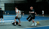 two men carrying tennis rackets on a tennis court with a bag that says babolat on it