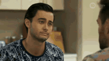 a man in a blue and white shirt is talking to another man in a kitchen