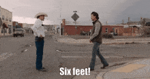two men standing on a street with the words six feet