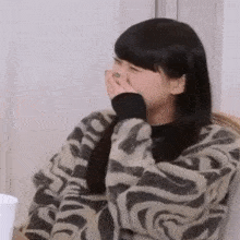 a woman in a zebra print sweater is covering her mouth with her hands .