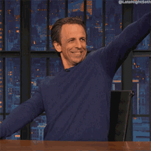 a man in a blue sweater is sitting at a table with his arm outstretched