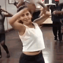 a woman in a white tank top is dancing in a dance studio with other people .