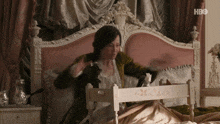 a woman is sitting on a bed with a tray in front of her that says hbo on the bottom