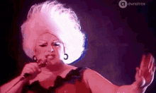 a drag queen is singing into a microphone while wearing a large pink wig .