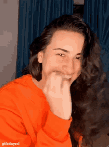 a woman with long hair wearing an orange sweater with the words gifsdayrol on the bottom