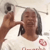a woman is making a funny face while wearing a white shirt and a fan behind her .