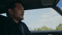 a man with a mustache is sitting in the back seat of a car looking out the window .
